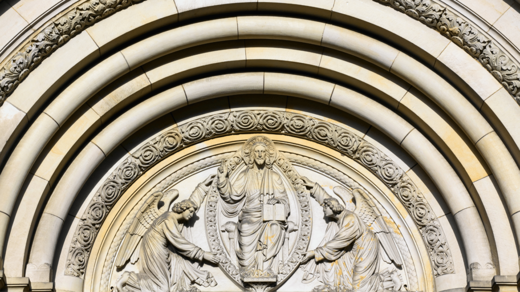 Relief sculpture of Christ with Alpha and Omega symbols surrounded by angels above an archway.