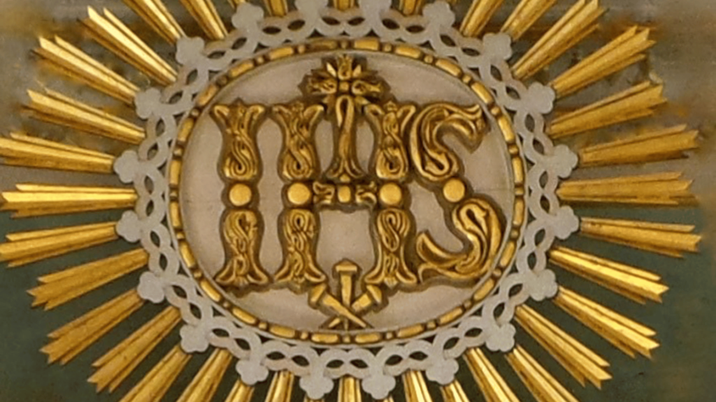 Ornate IHS symbol with golden rays.

