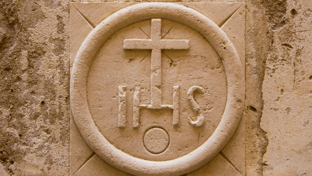 Stone carving of the IHS symbol with a cross.

